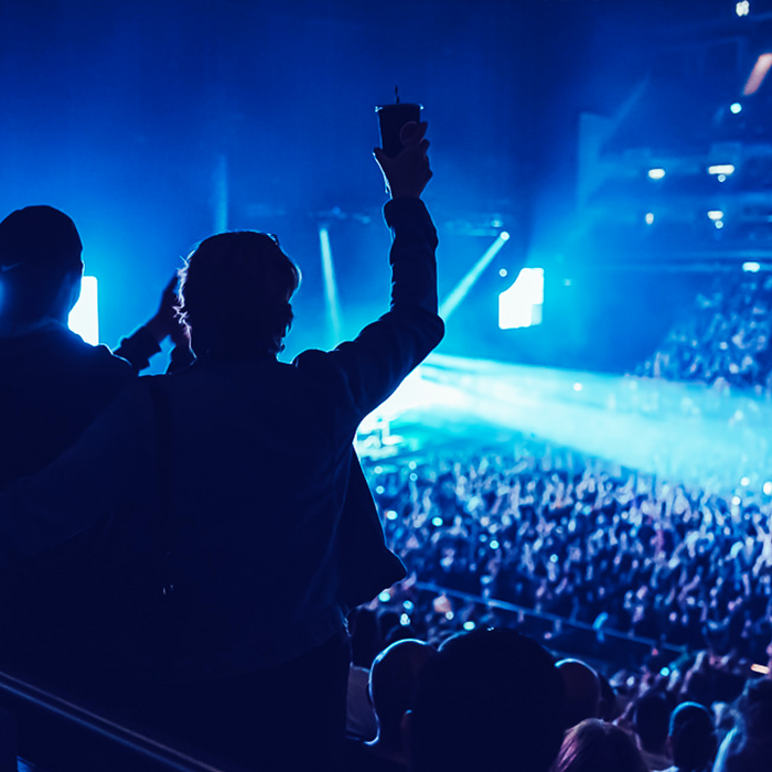 Image of silhoutte of a man with hands in the air against dark blue backdrop of The O2 
